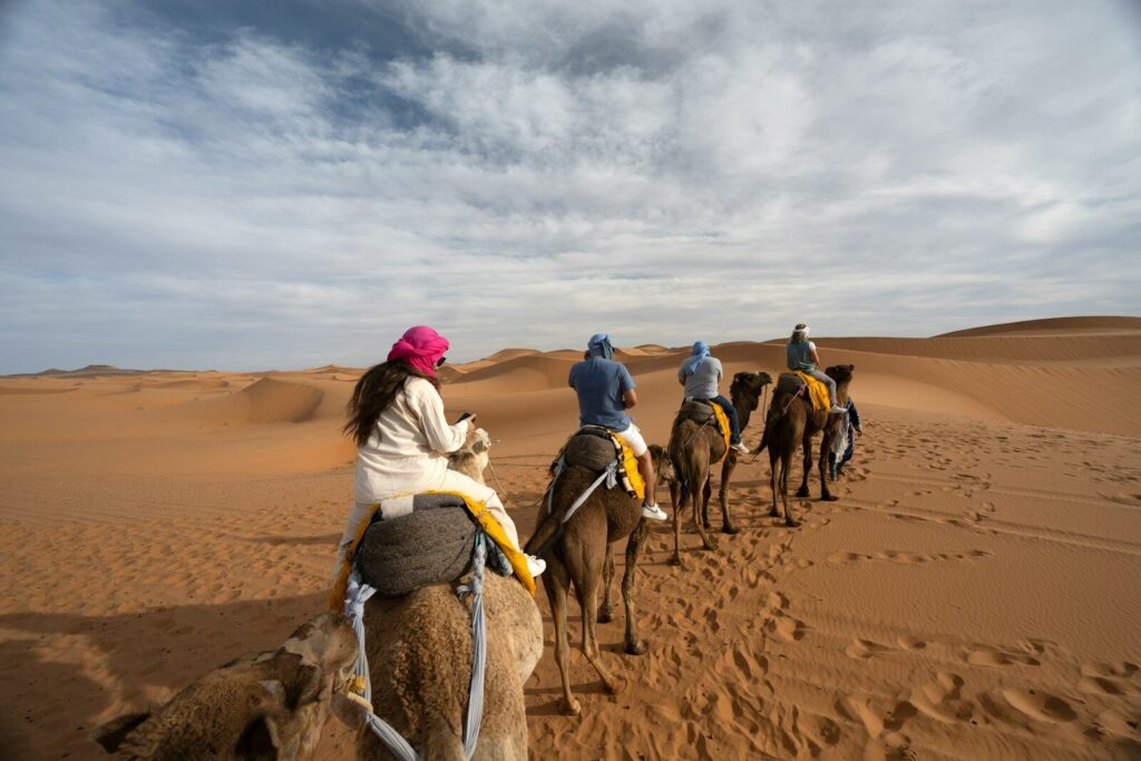 People ride camels across a desert landscape.